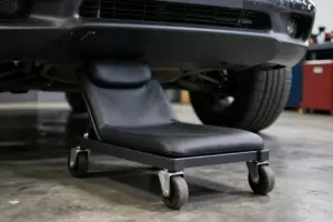 Ergonomic low-profile automotive creeper for under-car work resting on a polished garage floor beside a sports car