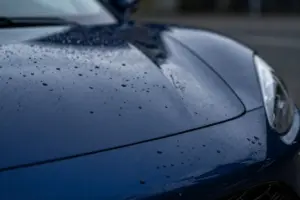 Macro shot of water beading on a dark blue sports car hood treated with ceramic coating spray for easy car detailing
