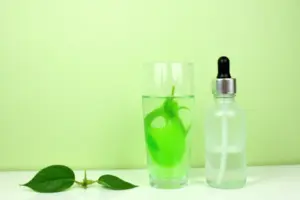 Green liquid chlorophyll drops being added to a glass of water beside fresh green leaves for natural internal deodorizing
