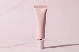 Sleek tube of glossy peptide lip treatment for plumping on a pastel pink marble surface